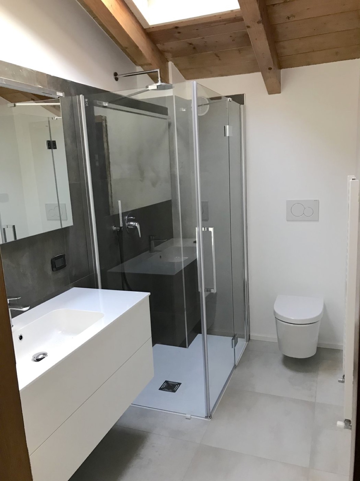 Bagno mansardato dopo l'intervento con doccia in vetro, sanitari sospesi e finiture contemporanee