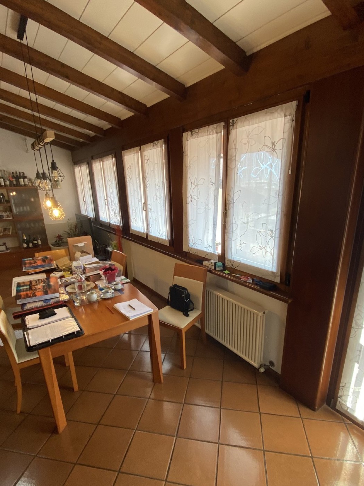 Zona living a Ceniga prima dell'intervento con pavimento datato, arredi tradizionali e travi in legno